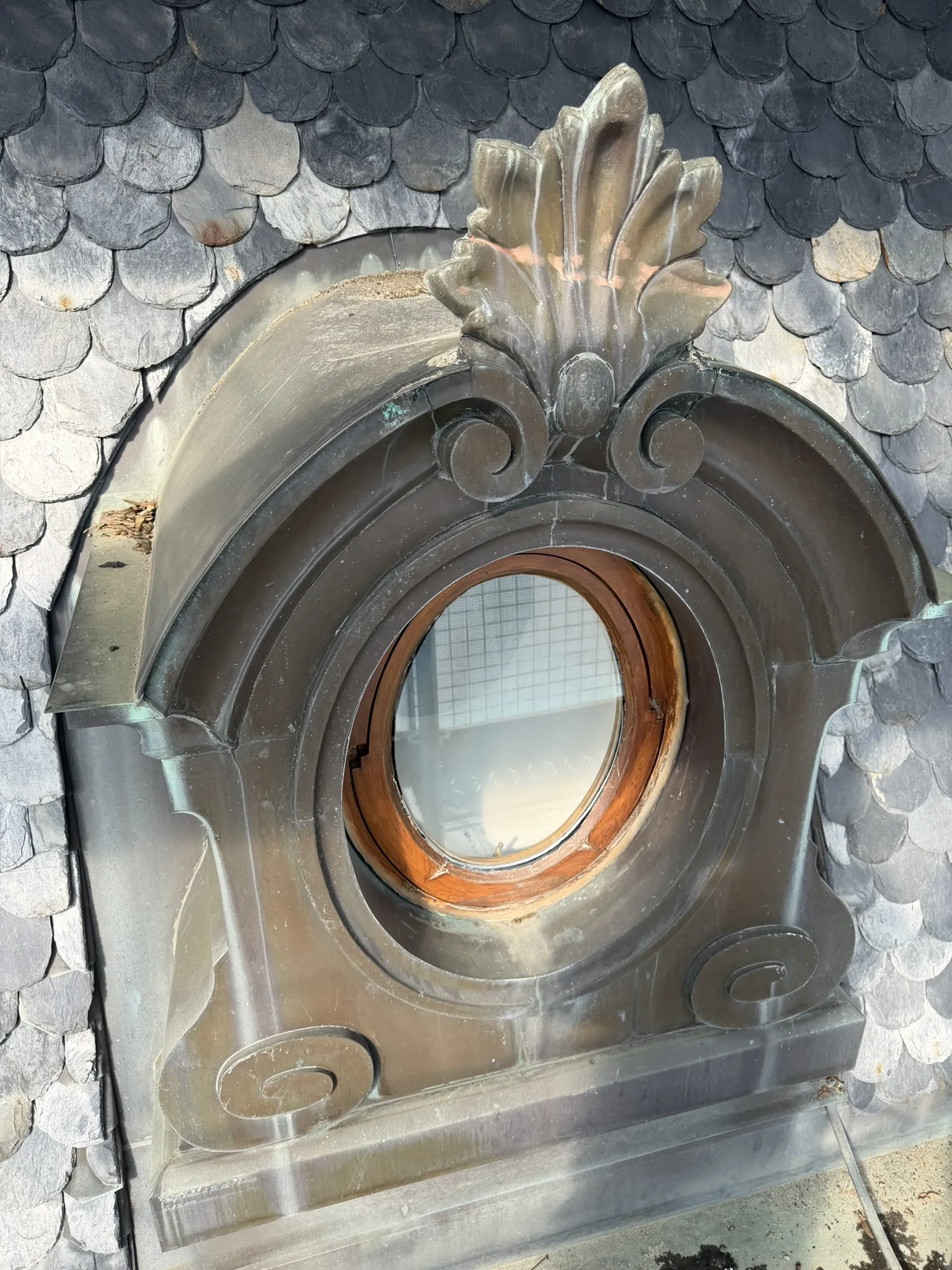 Oculus de pierre sculptée entouré d'une couverture en ardoise, sur un bâtiment classé.